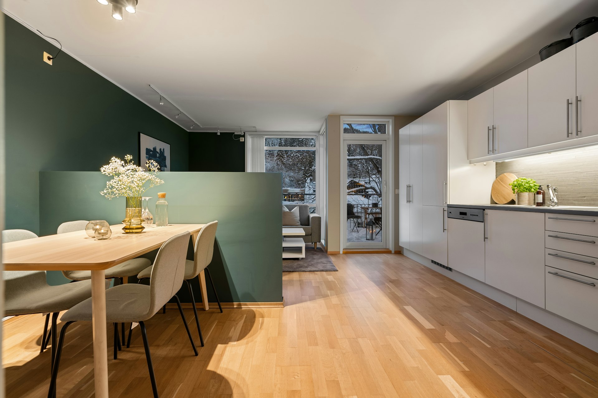 A room with a table and chairs and a kitchen in the background